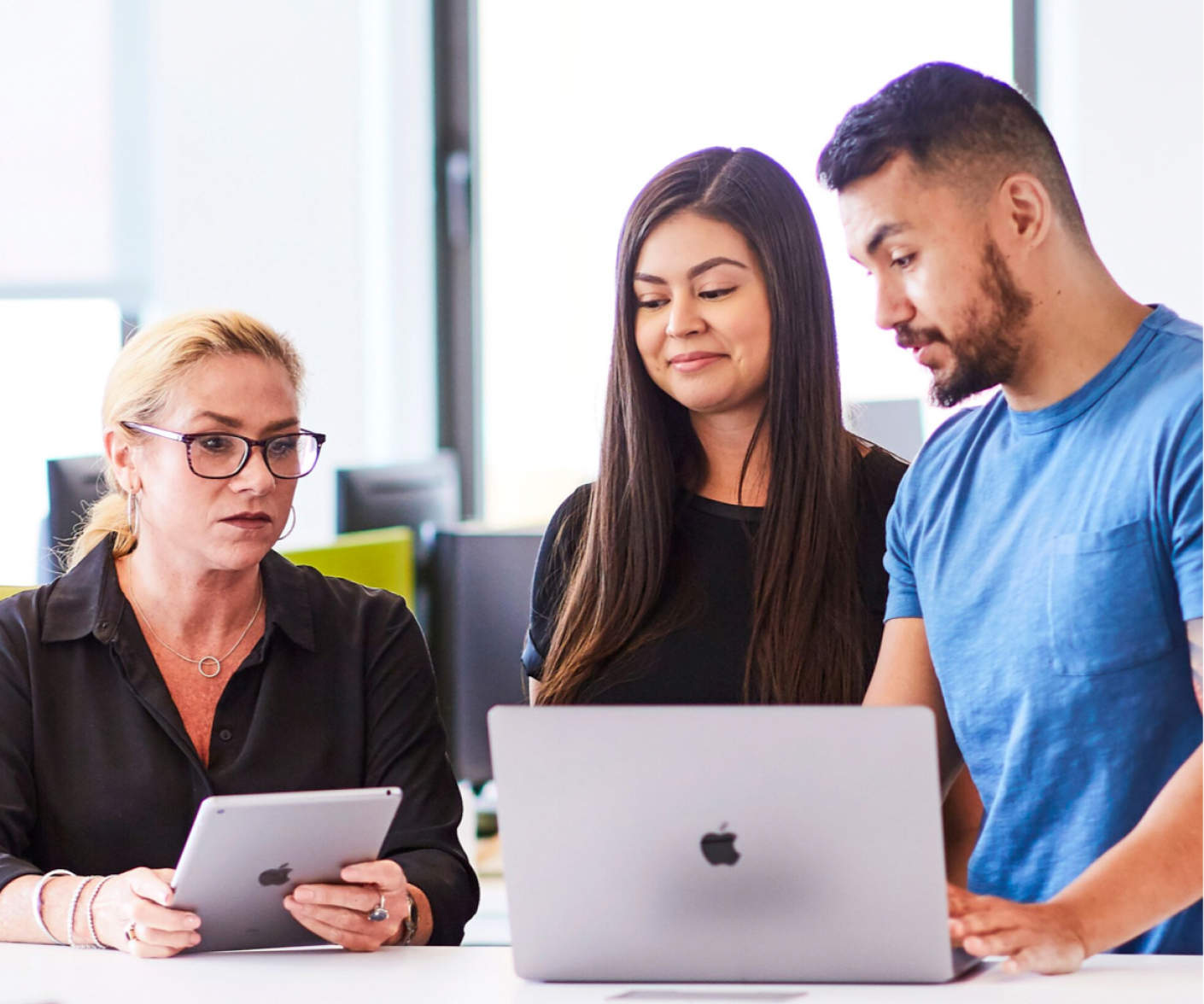 macos-kurs.de Drei Personen schauen in einem Büro auf einen Mac-Laptop.